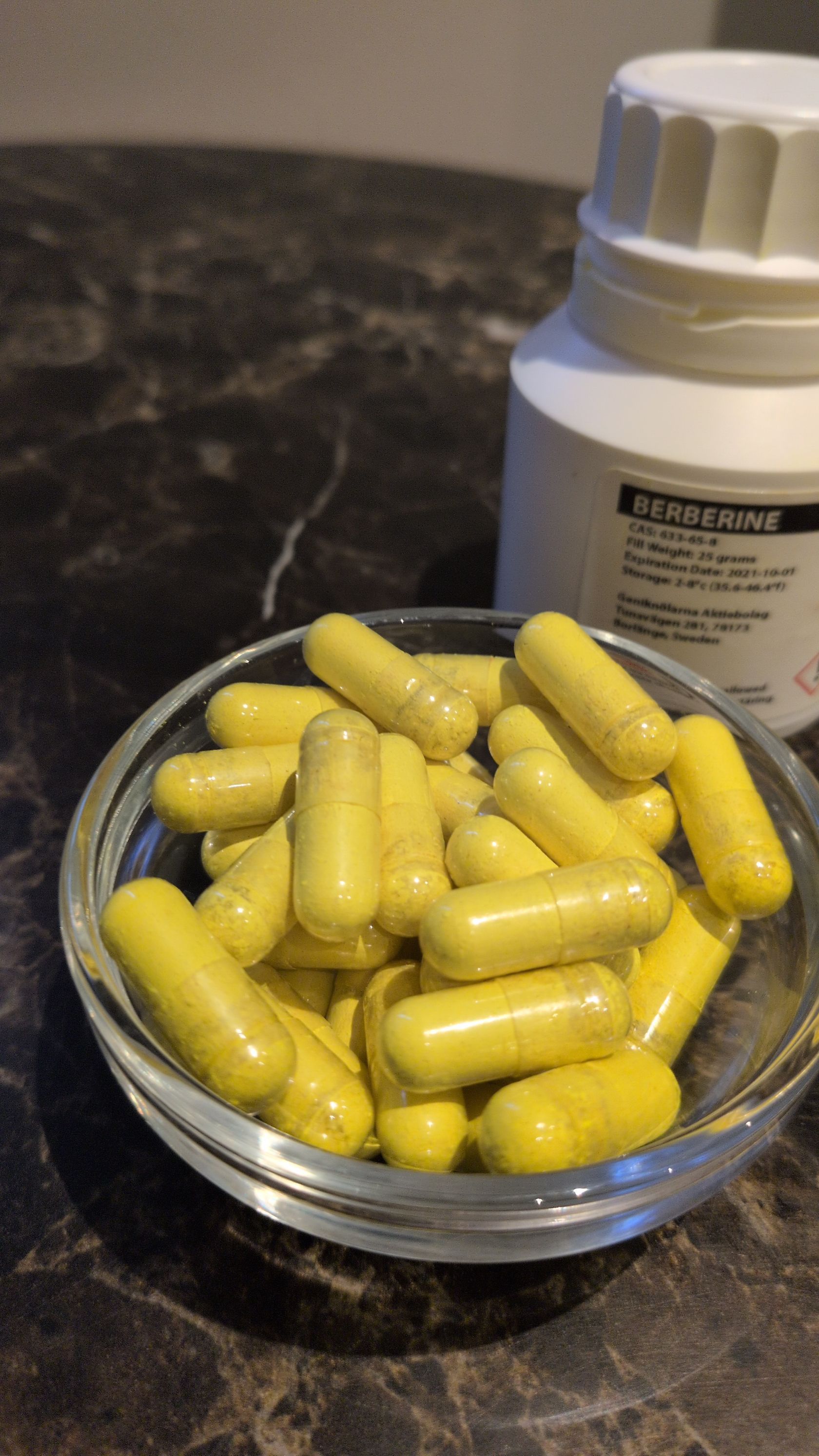 Berberīna kapsulas stikla bļodā blakus pudelei – skats no augšas