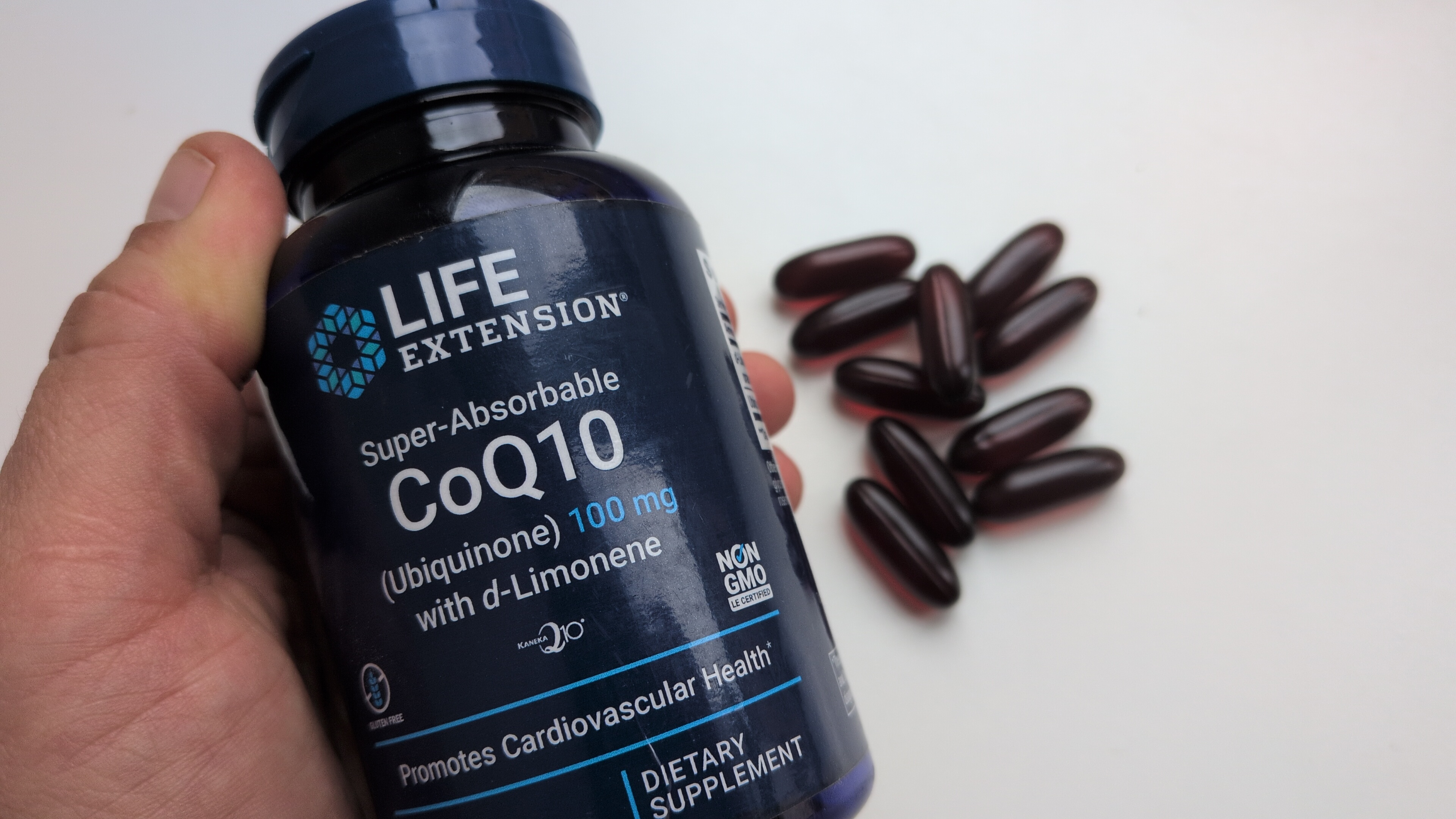 Roka tur Life Extension Super-Absorbable CoQ10 ubikvinona pudeli ar kapsulām blakus